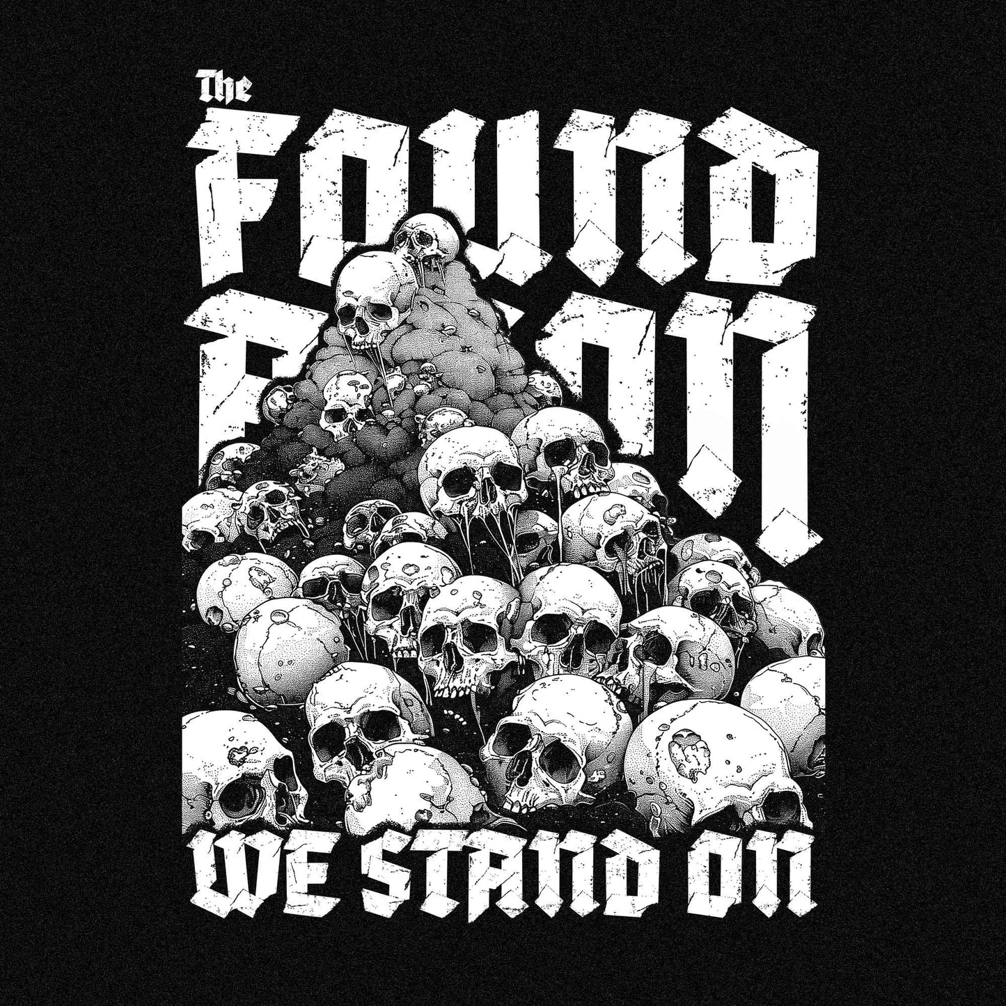 T-Shirt mit einem Berg aus Totenköpfen und dem Slogan 'The foundation we stand on'. Das Design ist Weiß auf schwarzem/dunkeln Stoff und thematisiert die brutalen Hintergründe von Landbesitz und Eroberung.