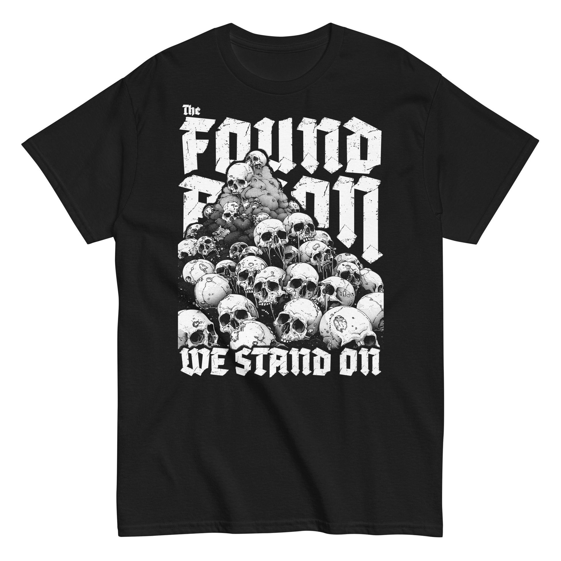 T-Shirt mit einem Berg aus Totenköpfen und dem Slogan 'The foundation we stand on'. Das Design ist Weiß auf schwarzem/dunkeln Stoff und thematisiert die brutalen Hintergründe von Landbesitz und Eroberung.